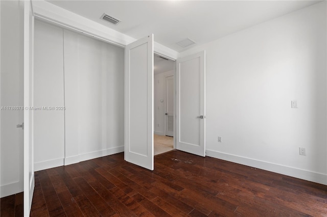 unfurnished bedroom with dark wood-type flooring, a closet, visible vents, and baseboards