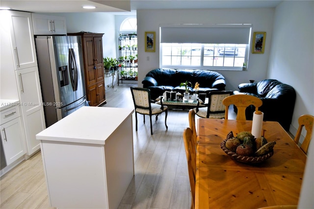 kitchen with light wood-style floors, stainless steel fridge, light countertops, white cabinets, and open floor plan
