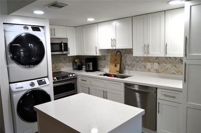 kitchen with a sink, visible vents, white cabinetry, stacked washer and dryer, and appliances with stainless steel finishes