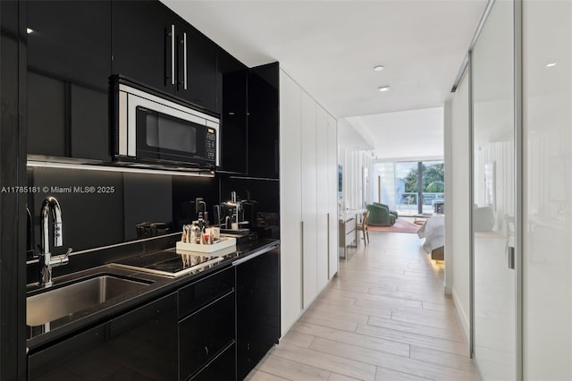 kitchen with stainless steel microwave, black electric stovetop, light wood-style flooring, a sink, and dark cabinets