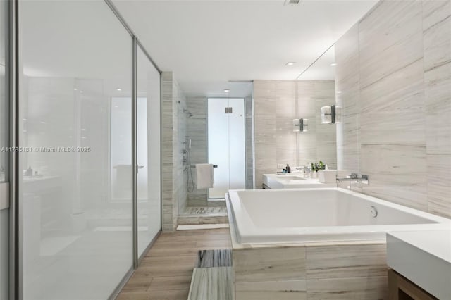 bathroom featuring a bathing tub, wood finished floors, vanity, and a stall shower