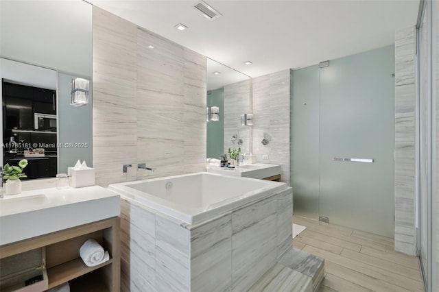 bathroom with a bath, tile walls, visible vents, and vanity