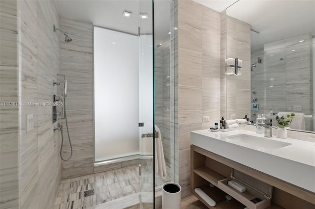 full bathroom with a stall shower, tile walls, and vanity