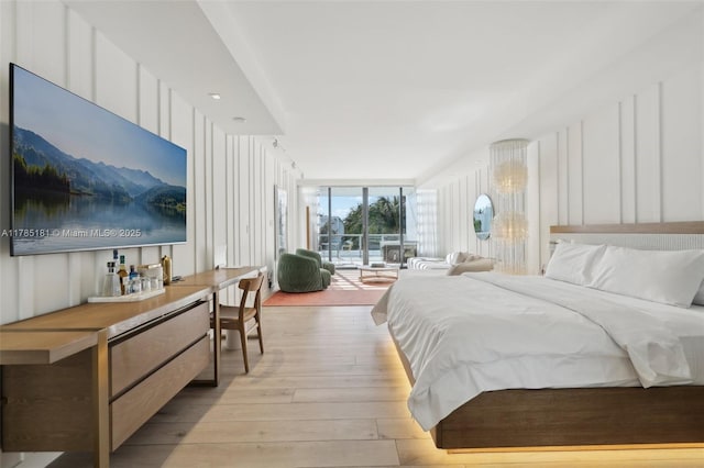 bedroom featuring light wood-type flooring, access to exterior, floor to ceiling windows, and a decorative wall