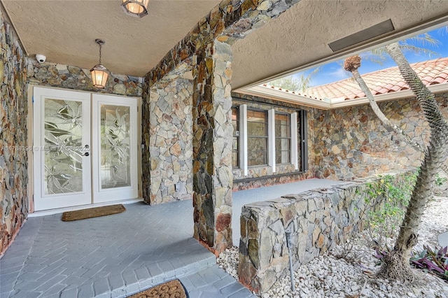doorway to property featuring french doors, stone siding, and a tiled roof