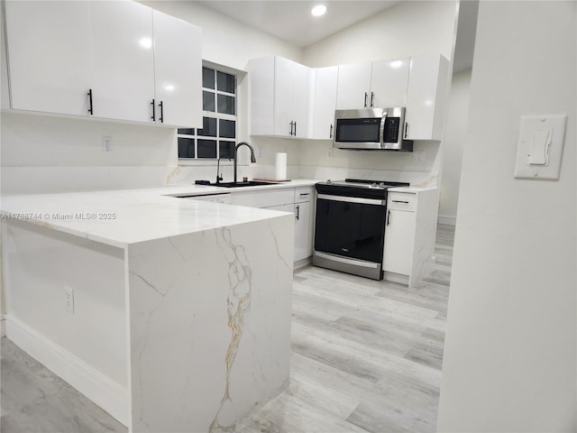 kitchen featuring range with electric stovetop, light stone counters, a sink, stainless steel microwave, and white cabinetry