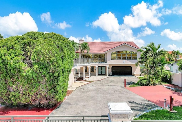 mediterranean / spanish home with a tile roof, a chimney, a garage, a balcony, and aphalt driveway