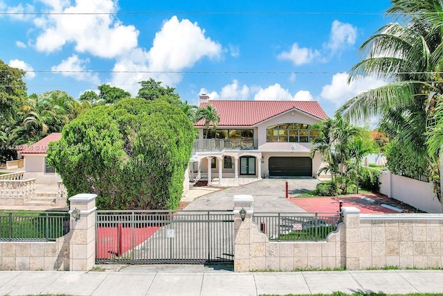 mediterranean / spanish-style house featuring a chimney, a fenced front yard, a tiled roof, a balcony, and an attached garage