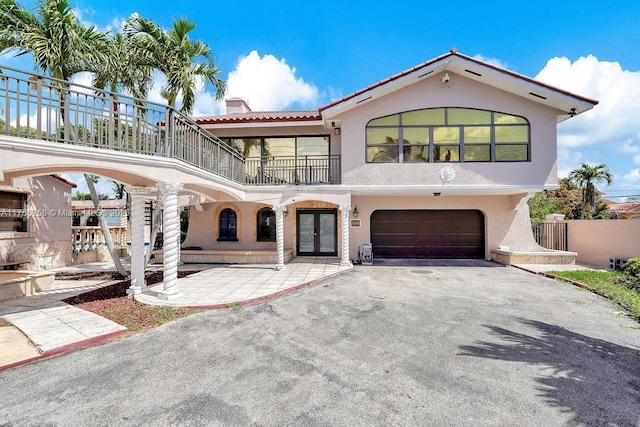 mediterranean / spanish house with aphalt driveway, a balcony, stucco siding, an attached garage, and french doors