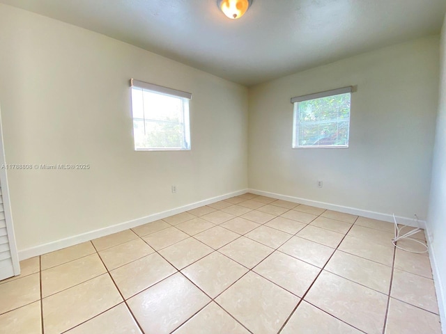 spare room featuring a wealth of natural light, light tile patterned flooring, and baseboards