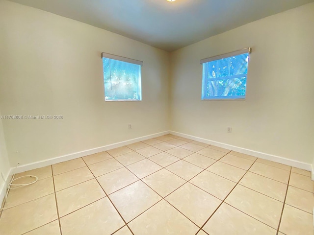 empty room featuring light tile patterned flooring, a wealth of natural light, and baseboards