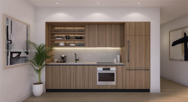 kitchen with black electric cooktop, light wood finished floors, oven, a sink, and decorative backsplash