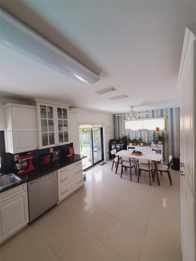 kitchen featuring dark countertops, dishwasher, light tile patterned floors, white cabinets, and glass insert cabinets