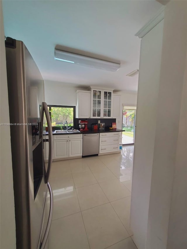 kitchen featuring dark countertops, appliances with stainless steel finishes, a sink, white cabinetry, and glass insert cabinets