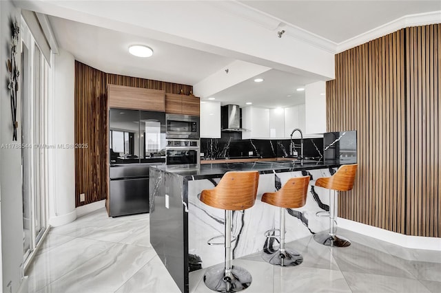 kitchen featuring wall chimney range hood, dark countertops, stainless steel appliances, and a breakfast bar