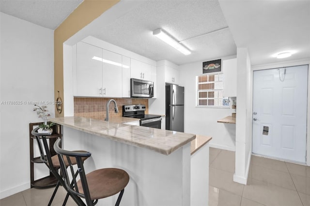 kitchen featuring decorative backsplash, a peninsula, appliances with stainless steel finishes, a breakfast bar area, and white cabinetry