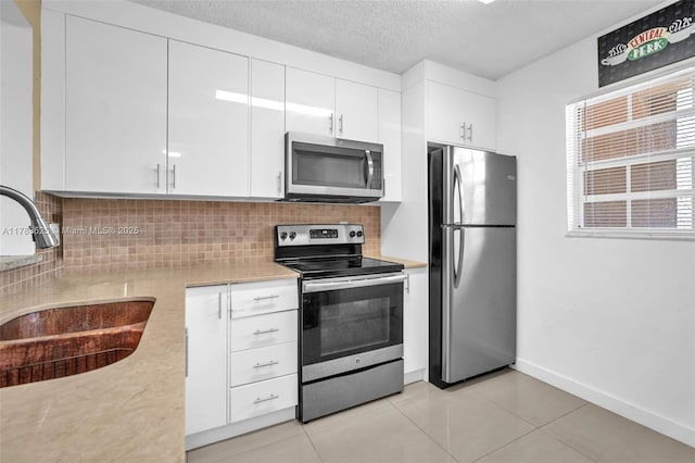 kitchen with white cabinets, stainless steel appliances, a sink, decorative backsplash, and light countertops