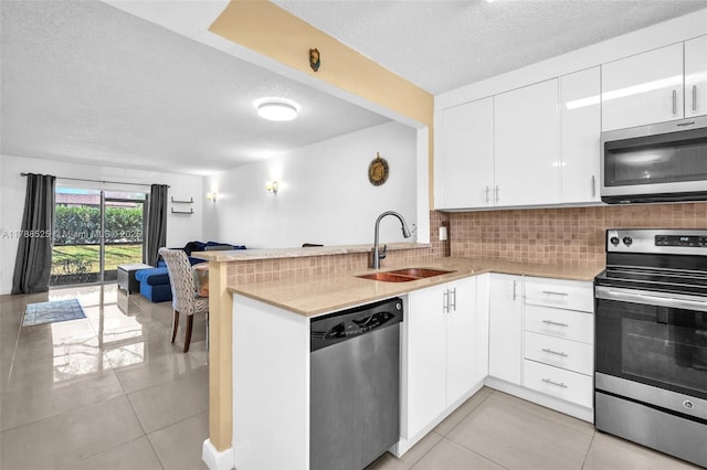 kitchen with stainless steel appliances, a sink, a textured ceiling, open floor plan, and backsplash