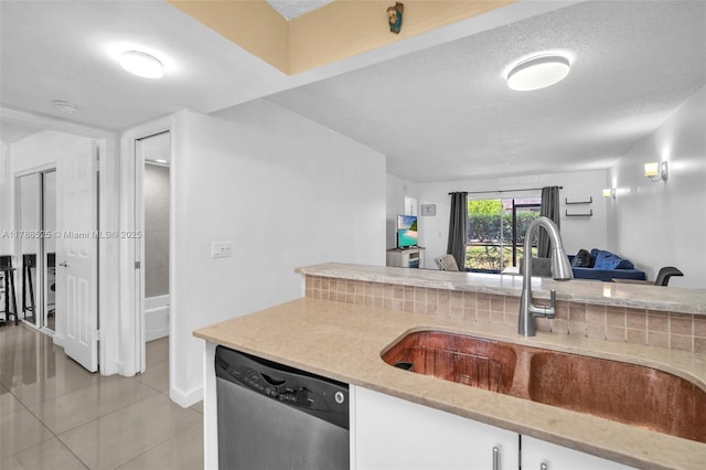 kitchen featuring stainless steel dishwasher, a sink, light tile patterned flooring, open floor plan, and white cabinetry