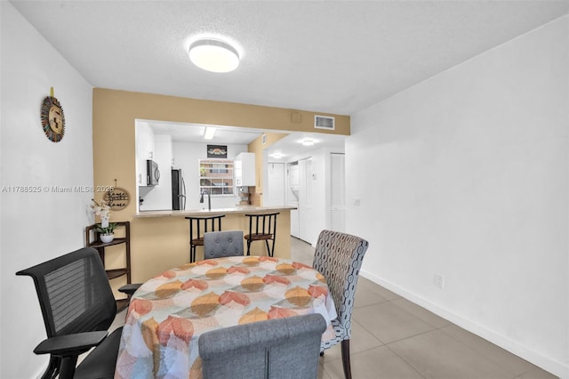 dining area with a textured ceiling, visible vents, baseboards, and light tile patterned floors