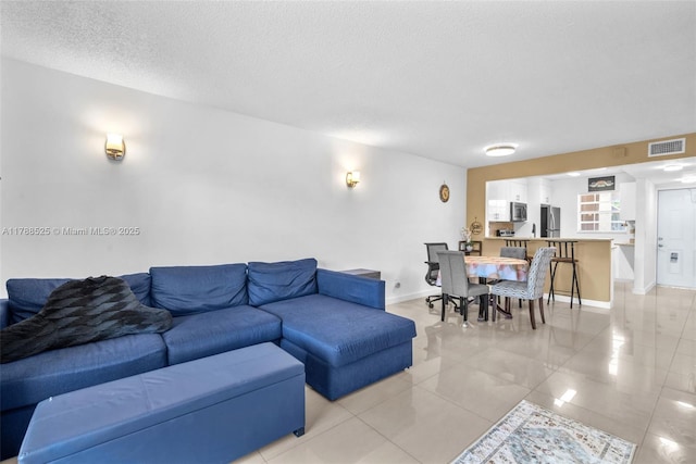 living area featuring baseboards, visible vents, a textured ceiling, and light tile patterned flooring
