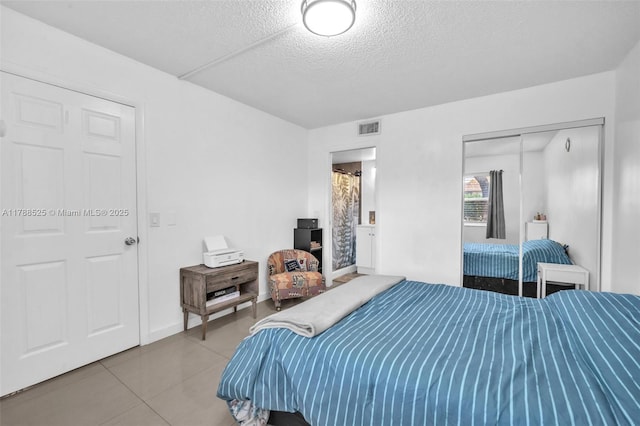 tiled bedroom featuring a textured ceiling, visible vents, and a closet