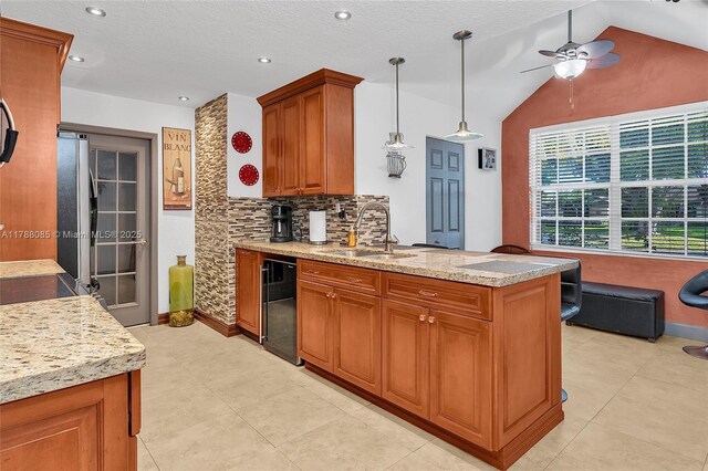 kitchen featuring a peninsula, a sink, backsplash, brown cabinets, and ceiling fan