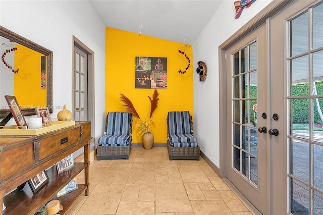 living area featuring lofted ceiling, stone tile floors, baseboards, and french doors