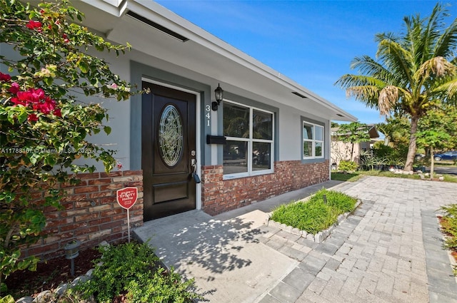 view of exterior entry with stucco siding and brick siding