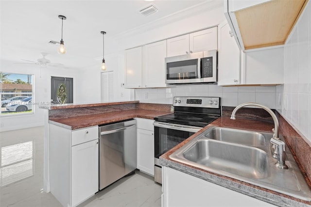 kitchen featuring white cabinets, stainless steel appliances, dark countertops, a sink, and a peninsula