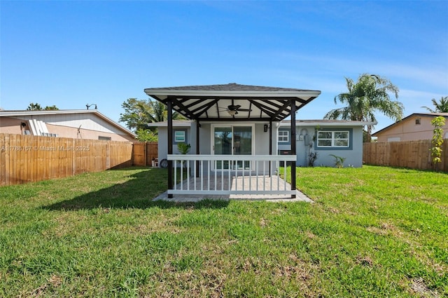 rear view of house with ceiling fan, a fenced backyard, a yard, and stucco siding