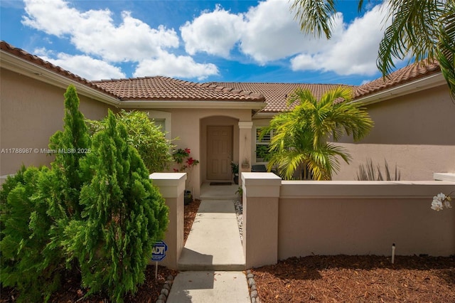 entrance to property with fence, stucco siding, and a tile roof