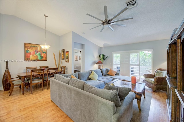 living room with vaulted ceiling, ceiling fan, light wood finished floors, visible vents, and a textured ceiling