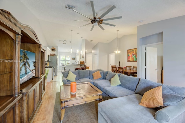 living area featuring visible vents, ceiling fan, lofted ceiling, and light wood finished floors