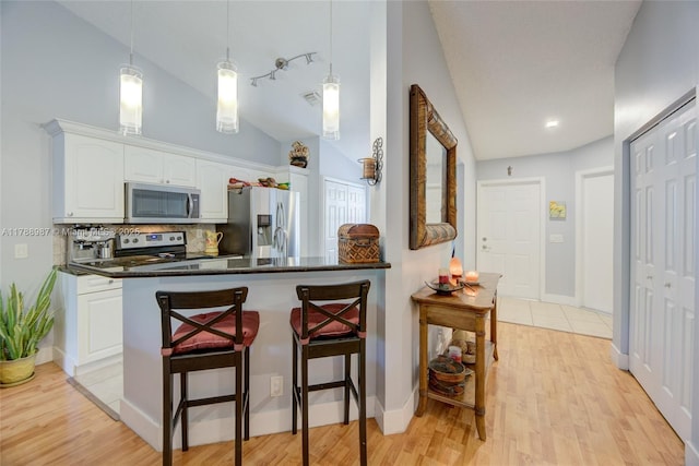 kitchen featuring a breakfast bar area, vaulted ceiling, backsplash, white cabinets, and appliances with stainless steel finishes