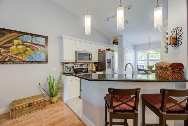 kitchen with stainless steel appliances, vaulted ceiling, backsplash, and white cabinetry