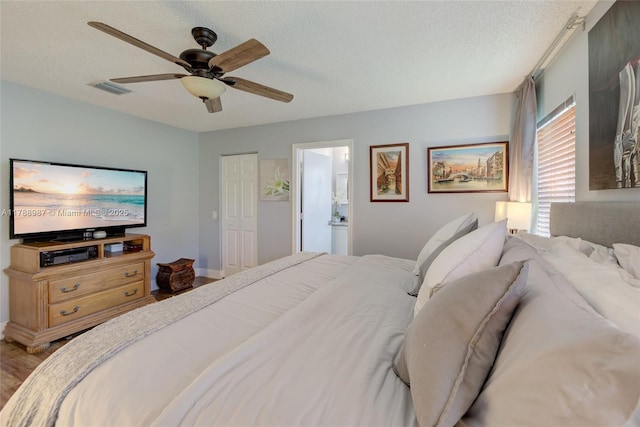 bedroom with wood finished floors, ensuite bath, ceiling fan, visible vents, and a textured ceiling