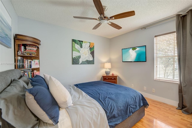 bedroom with a textured ceiling, wood finished floors, ceiling fan, and baseboards