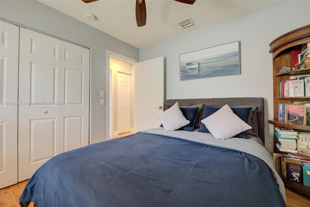 bedroom with a textured ceiling, visible vents, ceiling fan, a closet, and wood finished floors