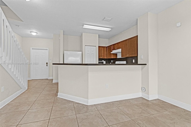 8308 Santa Monica Ave, Tamarac, FL 33321 - kitchen with freestanding refrigerator, under cabinet range hood, dark countertops, light tile patterned floors, and a peninsula