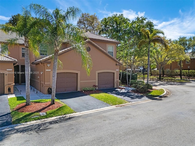 mediterranean / spanish house with a garage, a tiled roof, stucco siding, and aphalt driveway