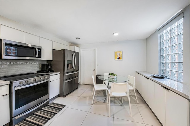 kitchen with stainless steel appliances, backsplash, white cabinetry, light countertops, and light tile patterned floors