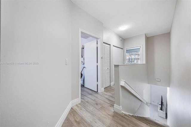 corridor featuring wood finished floors, baseboards, and an upstairs landing