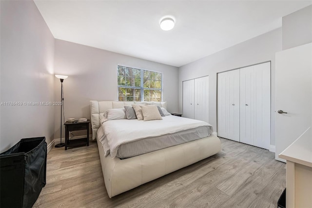 bedroom with two closets, baseboards, and light wood-style floors