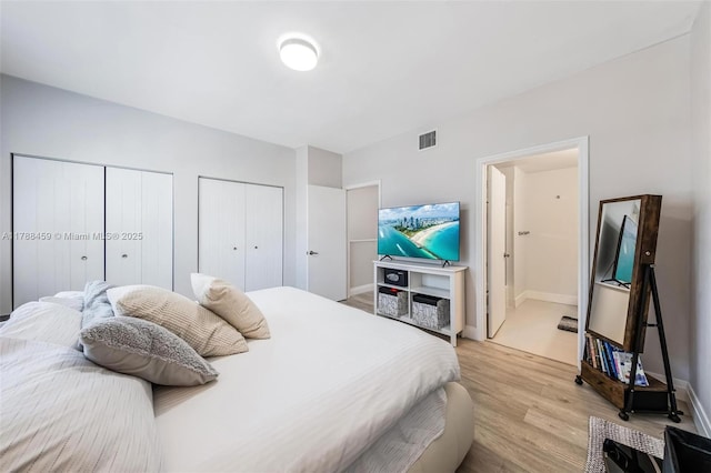 bedroom featuring baseboards, multiple closets, visible vents, and light wood-style floors