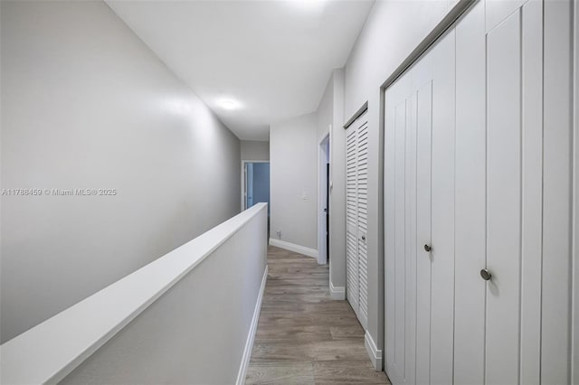 hallway featuring light wood-style floors, baseboards, and an upstairs landing