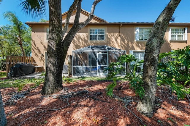 rear view of property featuring stucco siding, fence, a tiled roof, and glass enclosure