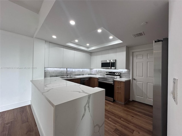 kitchen with a sink, stainless steel appliances, a peninsula, light stone countertops, and visible vents
