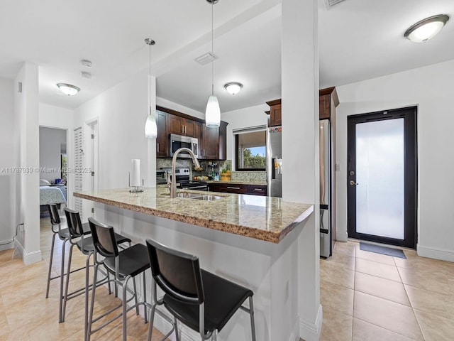 kitchen with a kitchen breakfast bar, dark brown cabinets, light stone countertops, baseboards, and appliances with stainless steel finishes