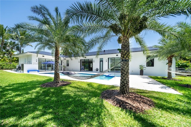 rear view of house with a patio area, an outdoor pool, a hot tub, a yard, and stucco siding